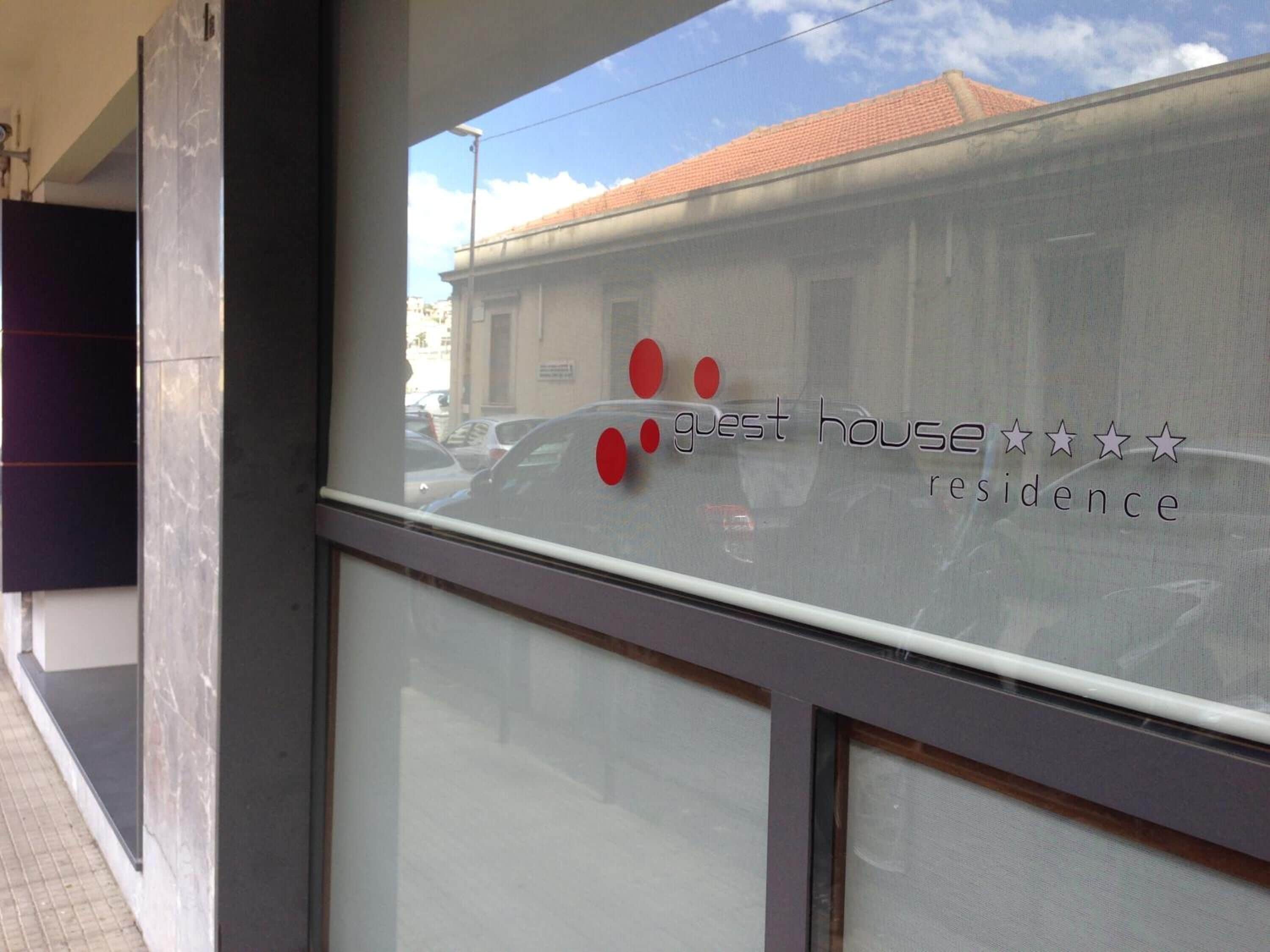 A window with a reflection of a building and a sign that reads "guest house residence".