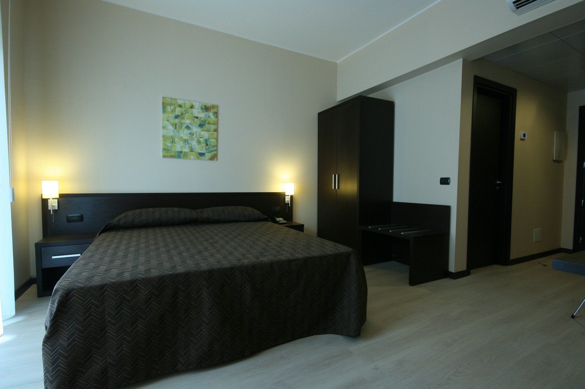 A hotel room with a large bed, two bedside tables with lamps, a wardrobe, and a painting on the wall.