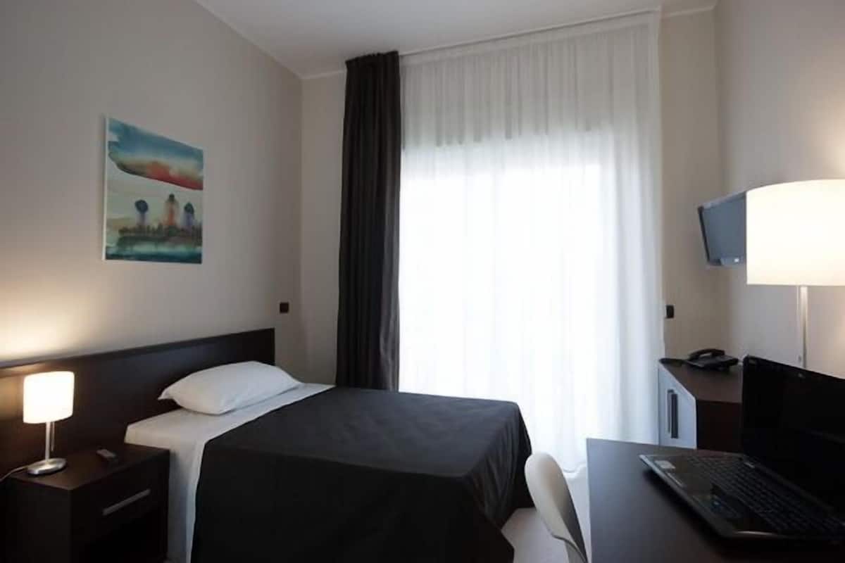 Une chambre d’hôtel avec un lit, un bureau avec un ordinateur portable, une télévision, une table de chevet avec une lampe et un tableau au mur.