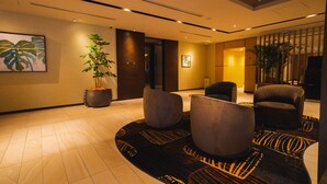 A lobby with a modern design, featuring a large potted plant, a seating area with two armchairs, and a patterned carpet. - Hotel Grand View Takasaki (Takasaki)