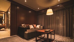 A modern living room with a dark brown sofa, a wooden coffee table, and a large window with curtains. - Hotel Grand View Takasaki (Takasaki)