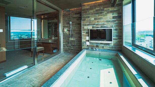 A modern bathroom with a large bathtub, a glass shower enclosure, and a TV mounted on the wall. - Hotel Grand View Takasaki (Takasaki)