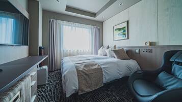 Habitación de hotel con cama, escritorio, sillón de masaje, televisor y ventana con cortinas.