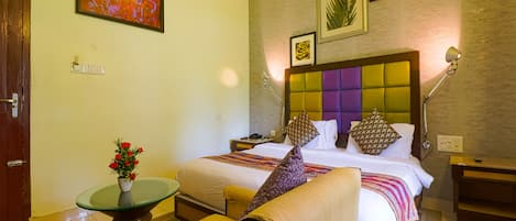 Habitación de hotel con una cama, una zona de estar con una silla, una mesita con un florero y una pared decorada con cuadros.