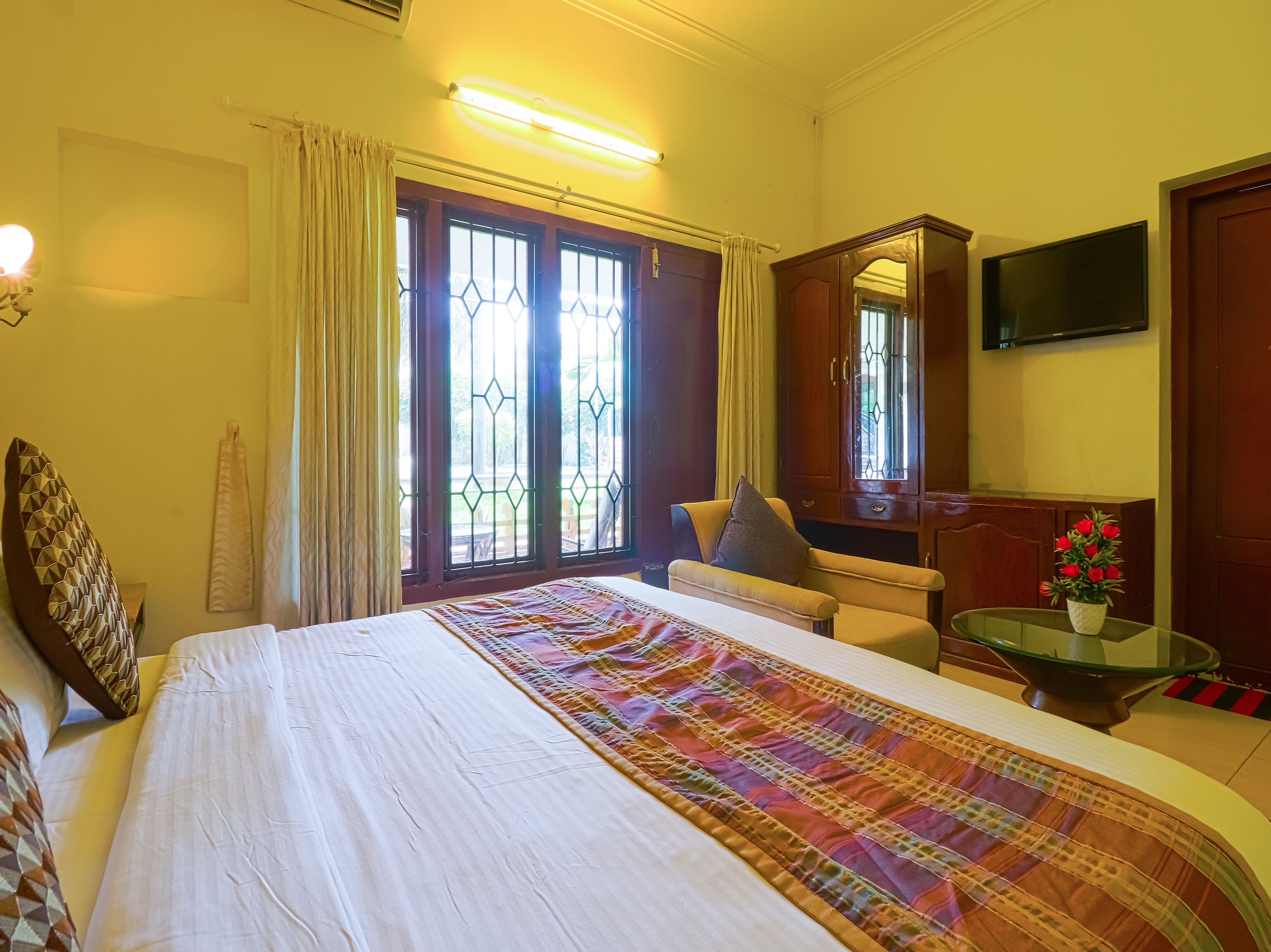 Une chambre d’hôtel avec un grand lit, un coin salon comprenant une chaise et une table, une télévision et une fenêtre avec des rideaux.