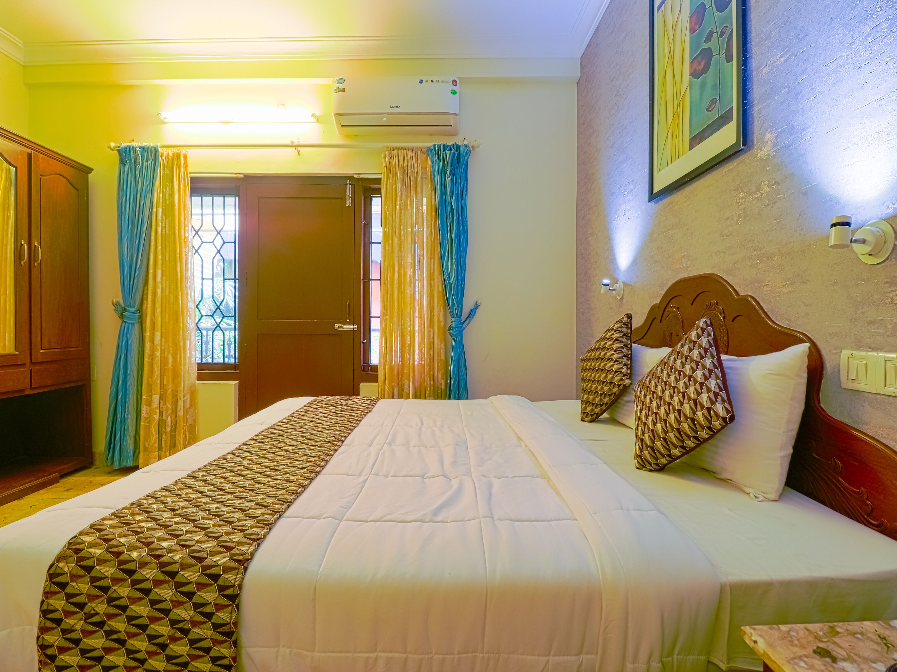 Habitación de hotel con una cama grande, cortinas, un armario de madera y un aire acondicionado de pared.