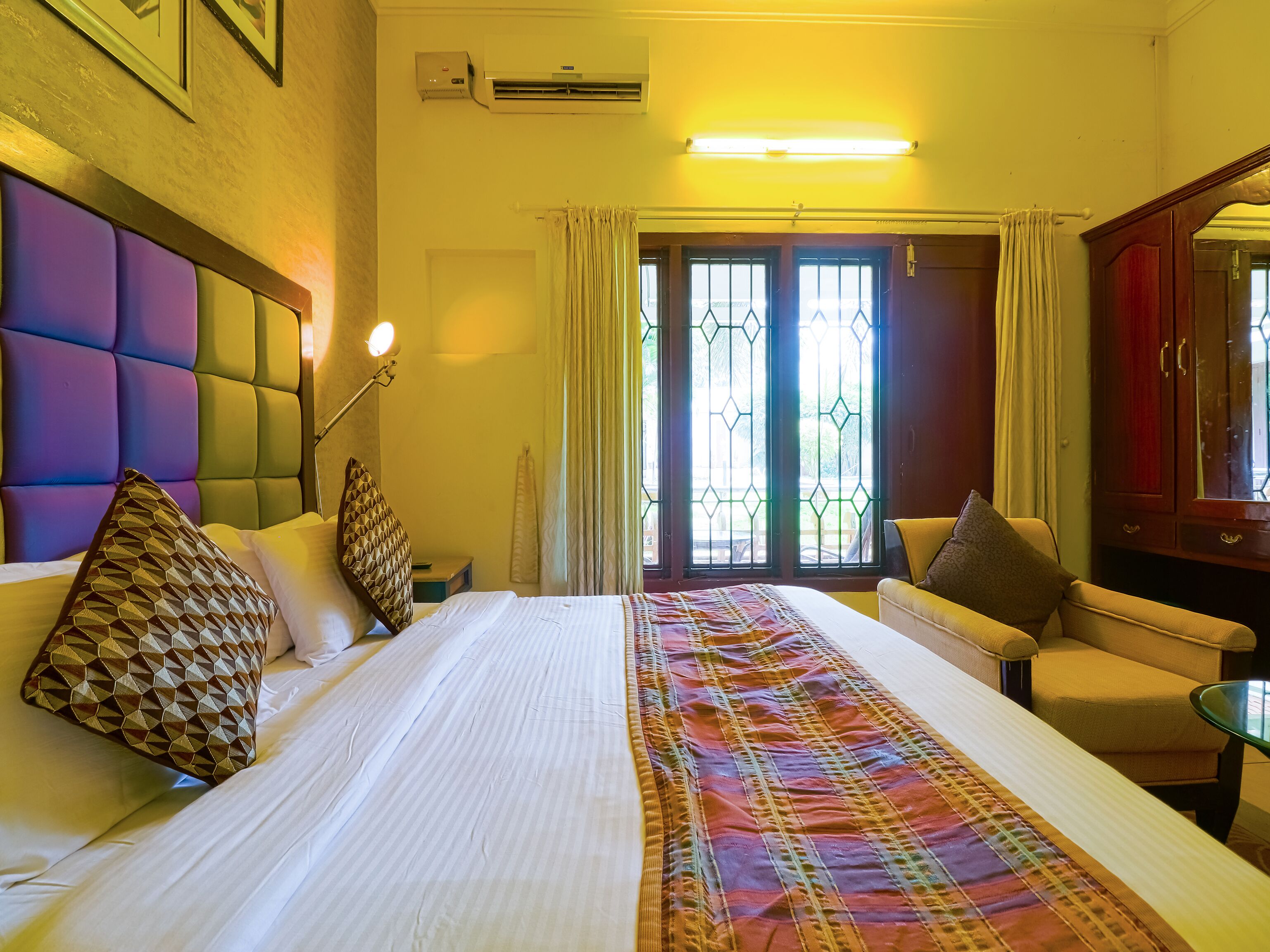 A hotel room with a large bed, a sofa, a small table, and a wardrobe.