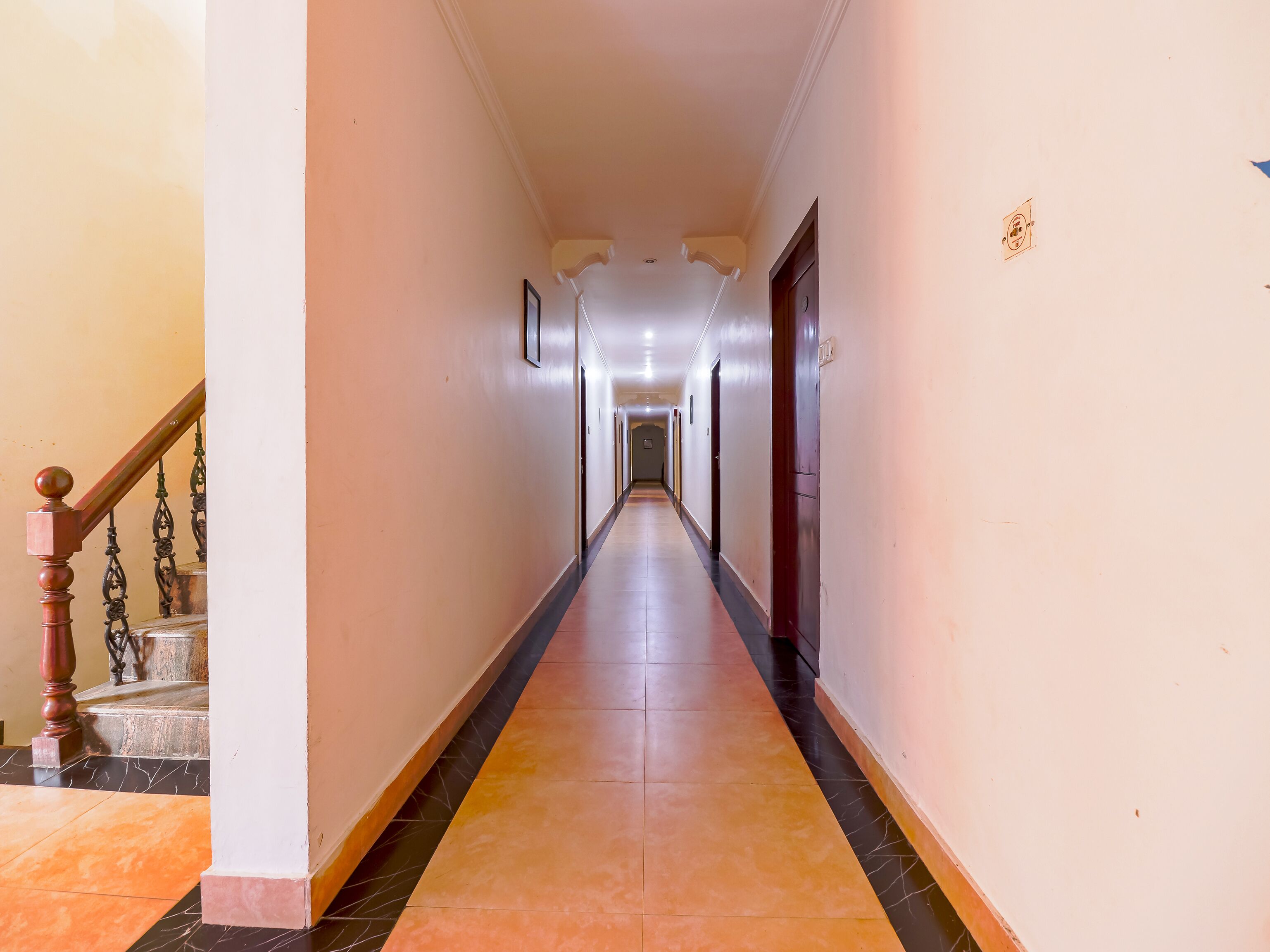 Um corredor comprido e estreito, com uma escadaria de madeira à esquerda e uma porta à direita.