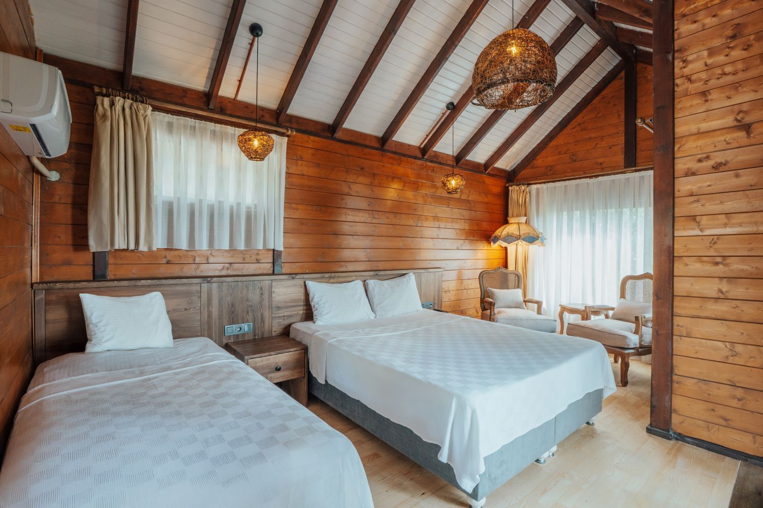A wooden cabin-style bedroom with two beds, a nightstand, a chair, and a lamp.
