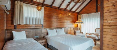 A wooden cabin-style bedroom with two beds, a nightstand, a chair, and a lamp.
