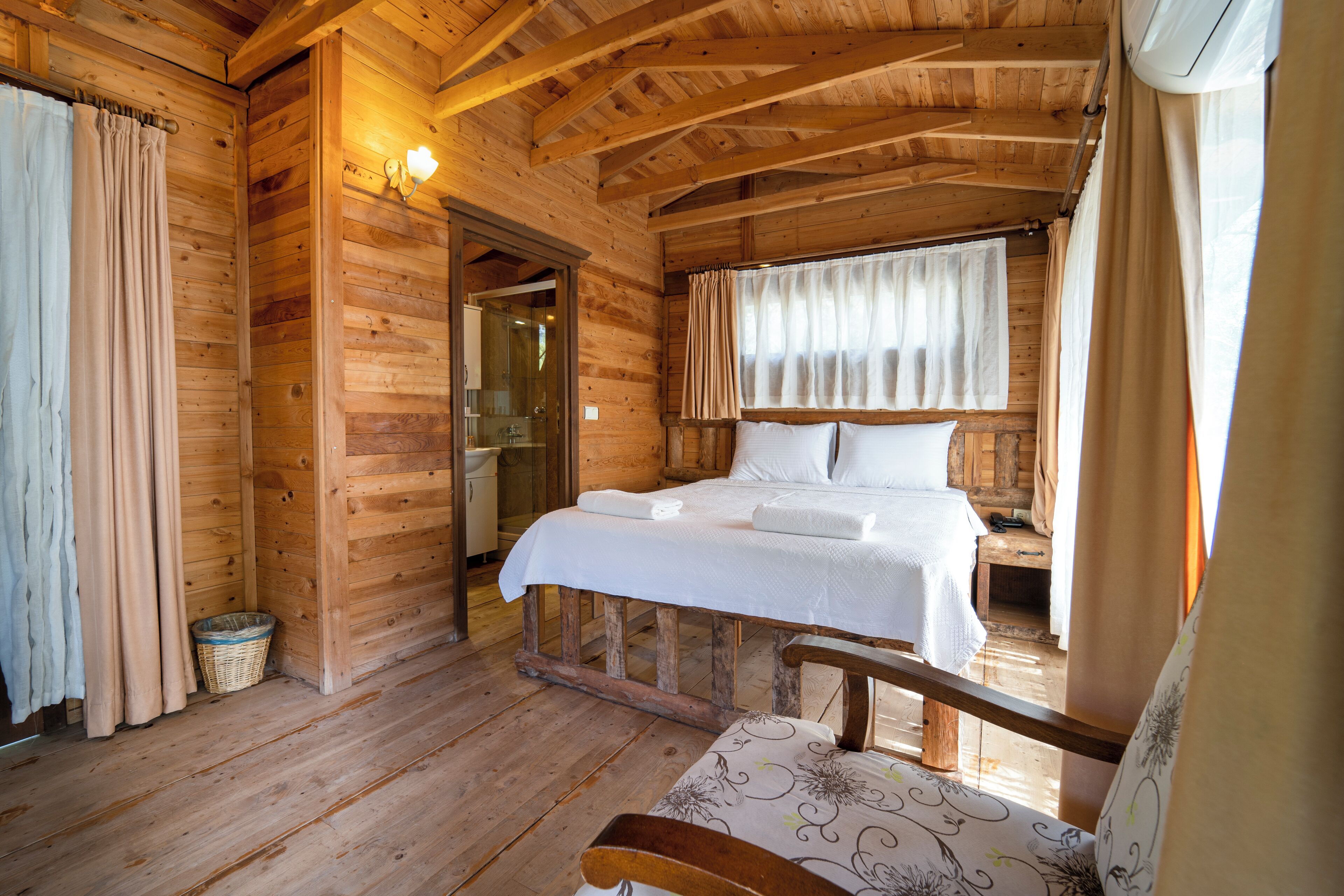 Een slaapkamer in een houten hutje, met een bed, een bankje en een kleine tafel.