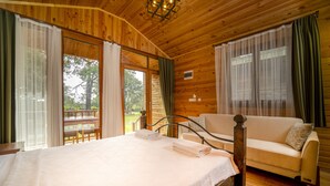 A wooden cabin bedroom with a bed, a sofa, and a balcony. - Sea Valley Lodge (Fethiye)