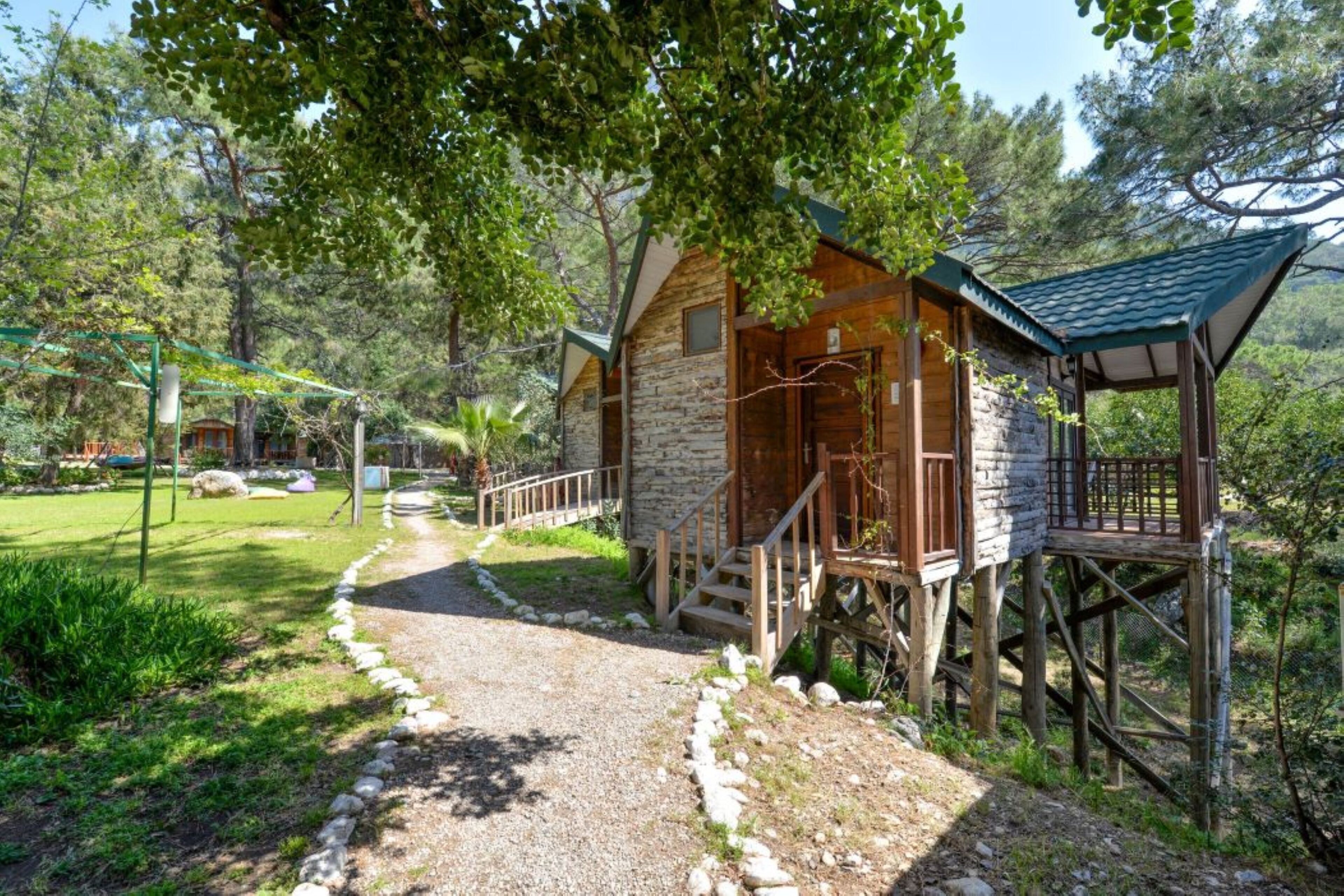 A rustic cabin with a stone exterior, wooden deck, and a gravel path leading to it.