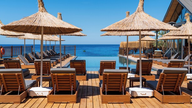 A wooden deck with lounge chairs and thatched umbrellas overlooking a pool and the sea. - Sea Valley Lodge (Fethiye)