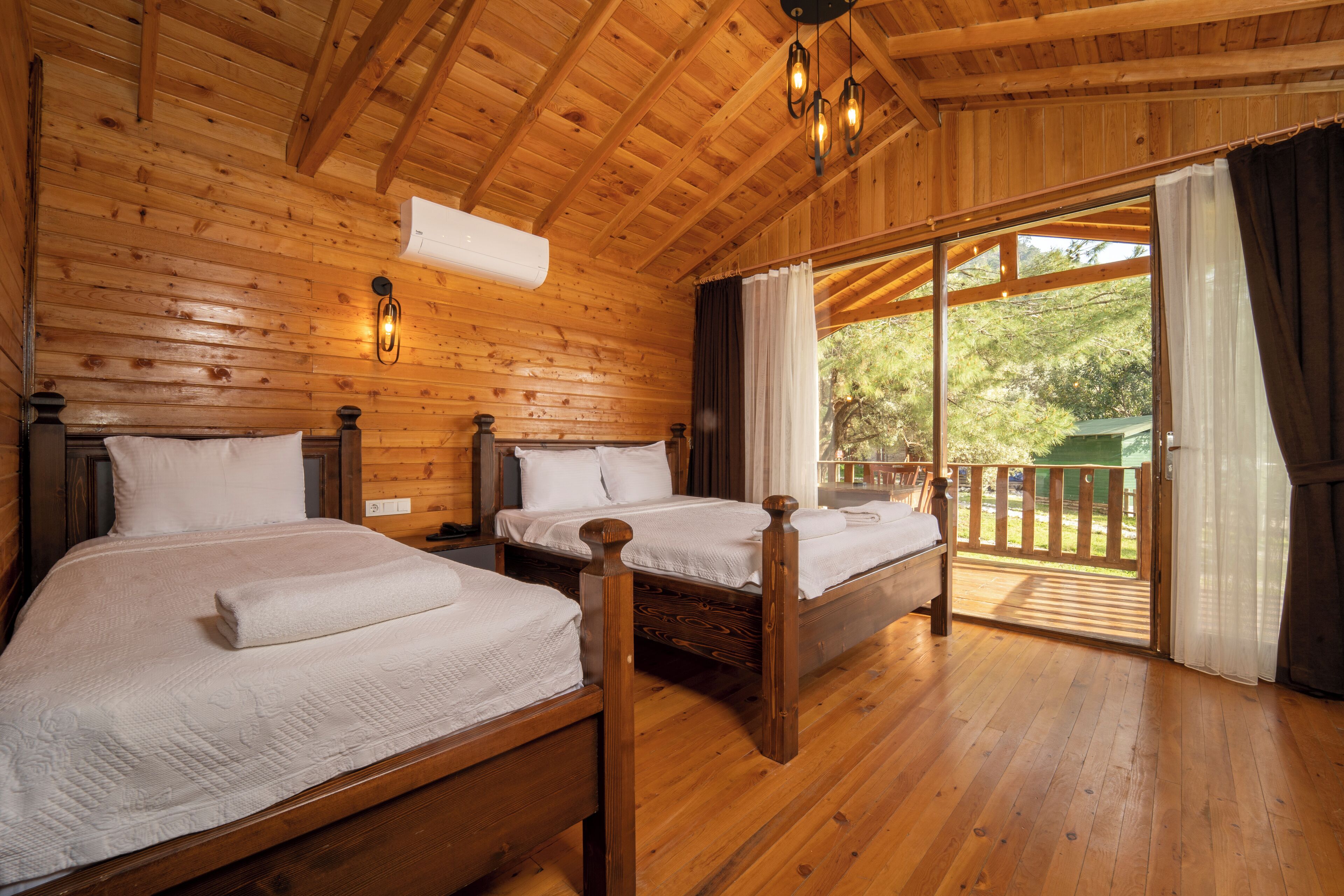 A wooden cabin room with two beds, a balcony, and a large window.