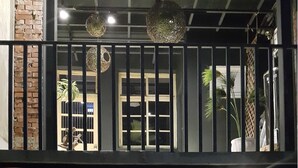 Un edificio de dos pisos con fachada negra y un frente de cristal. La planta baja tiene un área de estar con mesas y sillas. El piso superior cuenta con un balcón con luces colgantes.