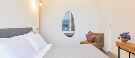 Un dormitorio con una cama grande, un pequeño rincón de descanso, un espejo y vistas al mar.