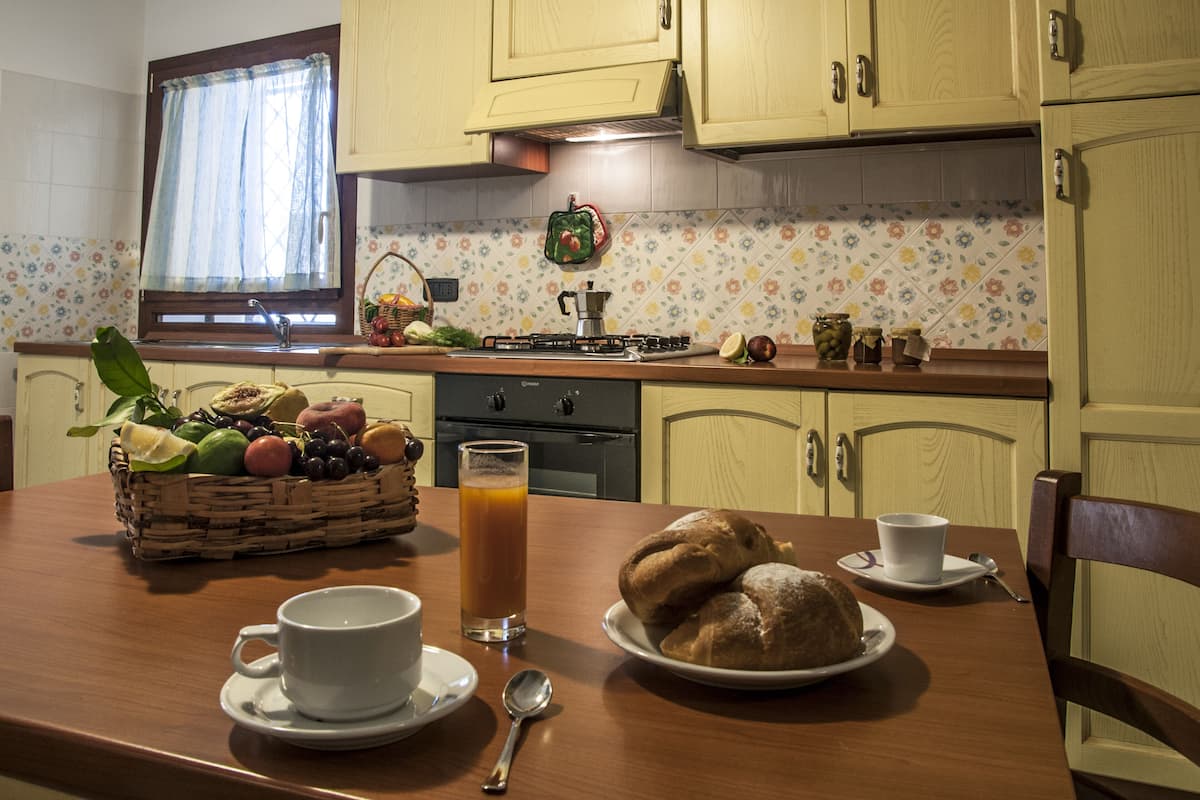 Eine Küche mit einem Holztisch, gedeckt für ein Frühstück, inklusive einer Obstkorb, einem Gebäckteller, einer Tasse und einem Glas Saft.