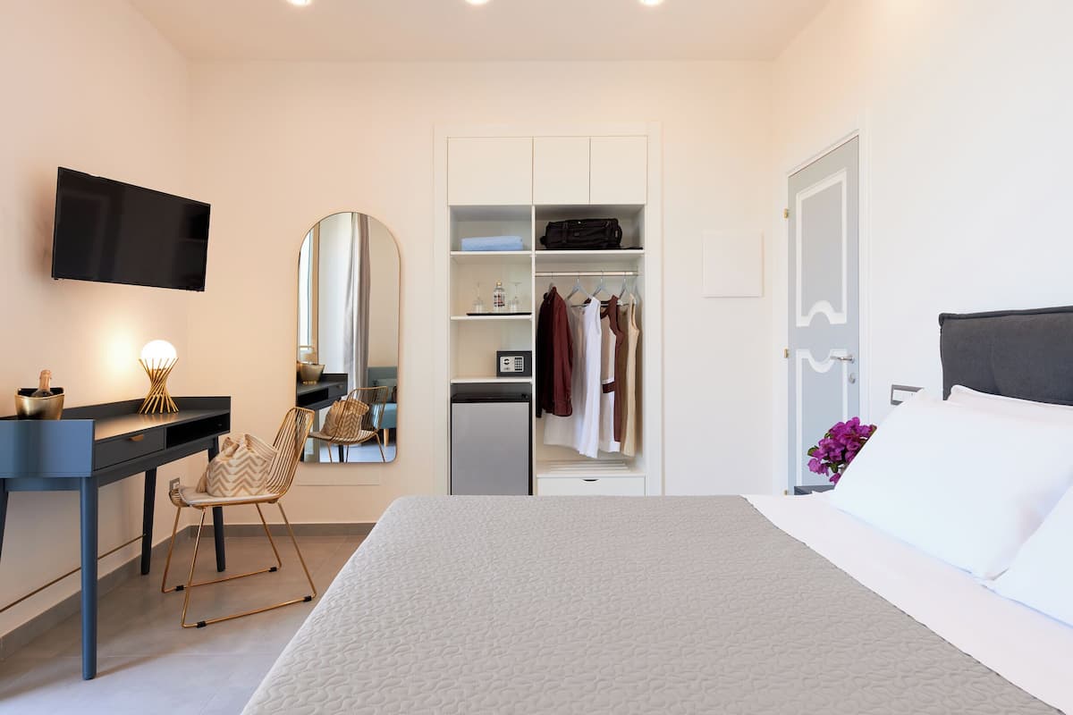 Ein Hotelzimmer mit Bett, Schreibtisch mit Stuhl, Kleiderschrank, Spiegel und Fernseher.