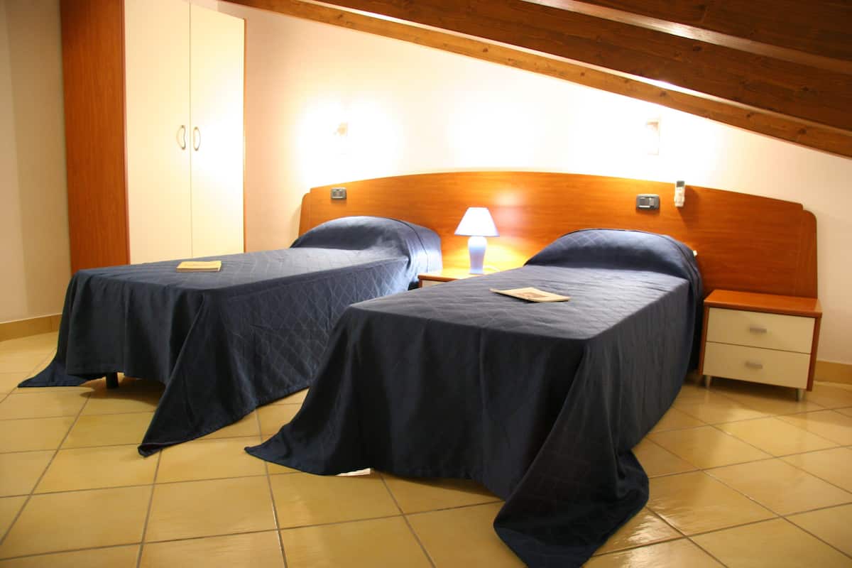Ein Zimmer mit zwei Einzelbetten, einem Holzkopfteil, einem Nachttisch mit Lampe und einem Kleiderschrank.