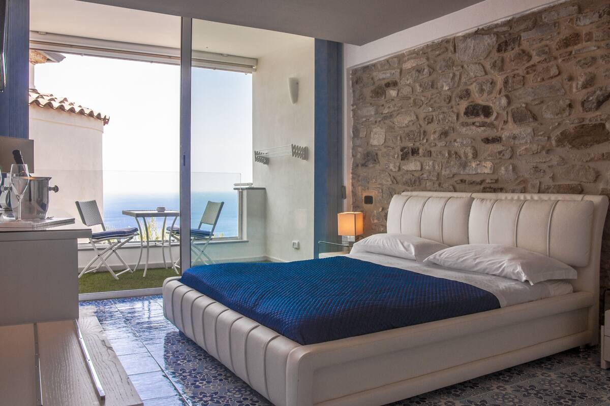 Ein Schlafzimmer mit Bett, Schreibtisch, Stuhl, Lampe und Meerblick.
