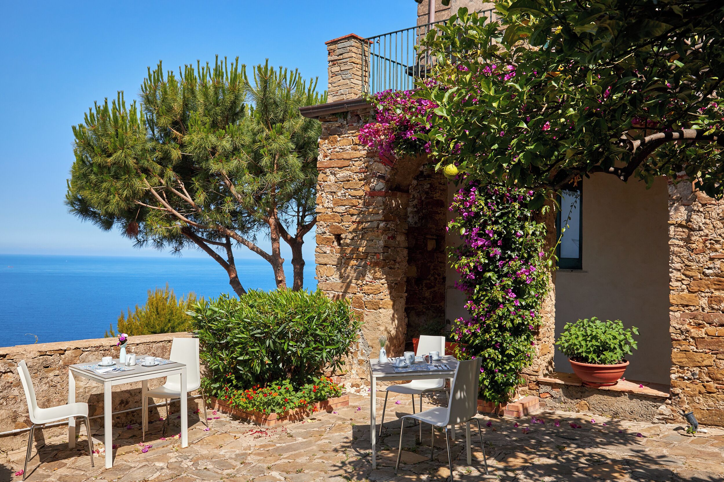 Une terrasse avec deux tables dressées pour le dîner, offrant une vue panoramique sur la mer.