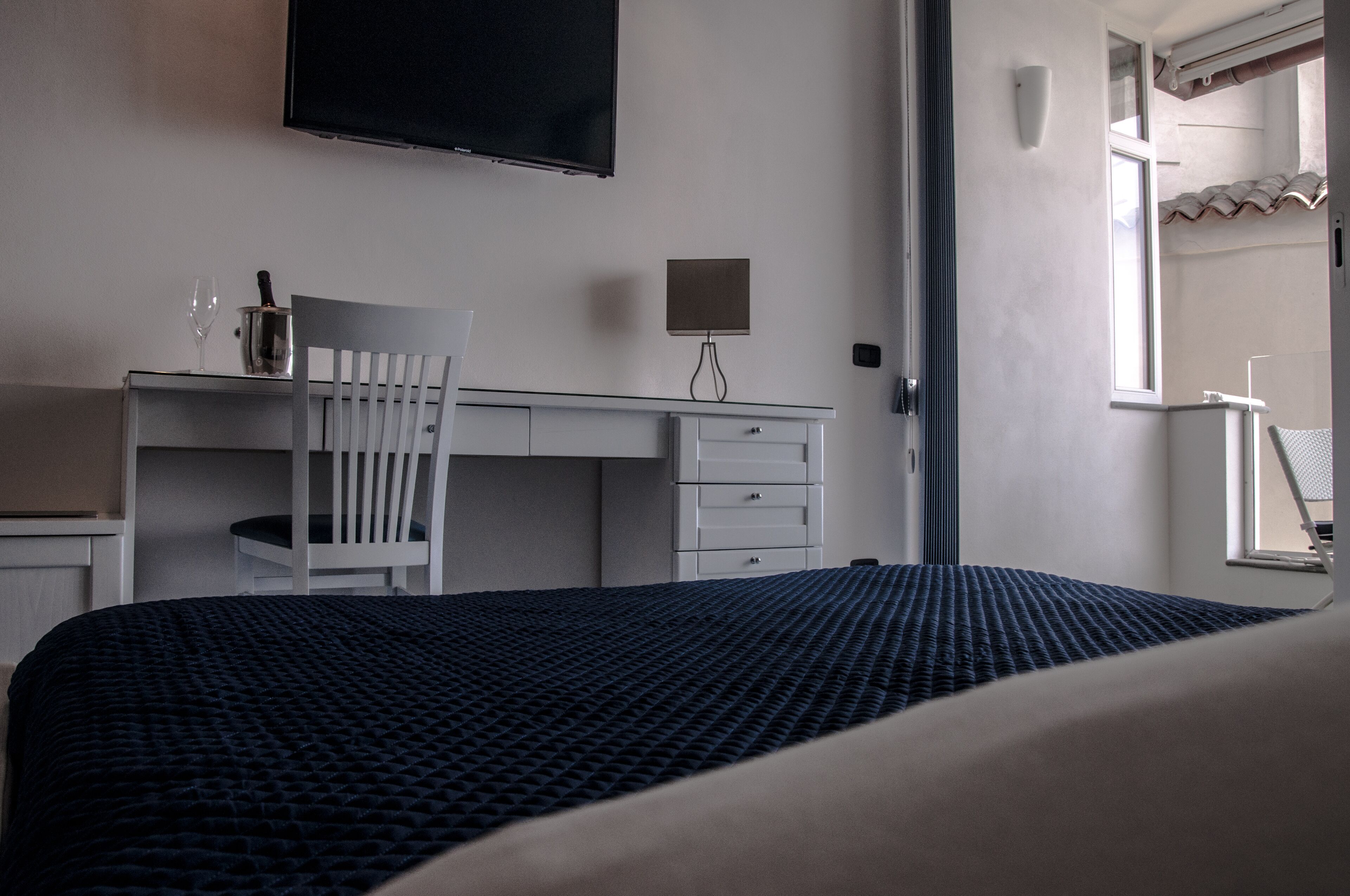 A hotel room with a bed, a desk, a chair, a TV mounted on the wall, and a window.