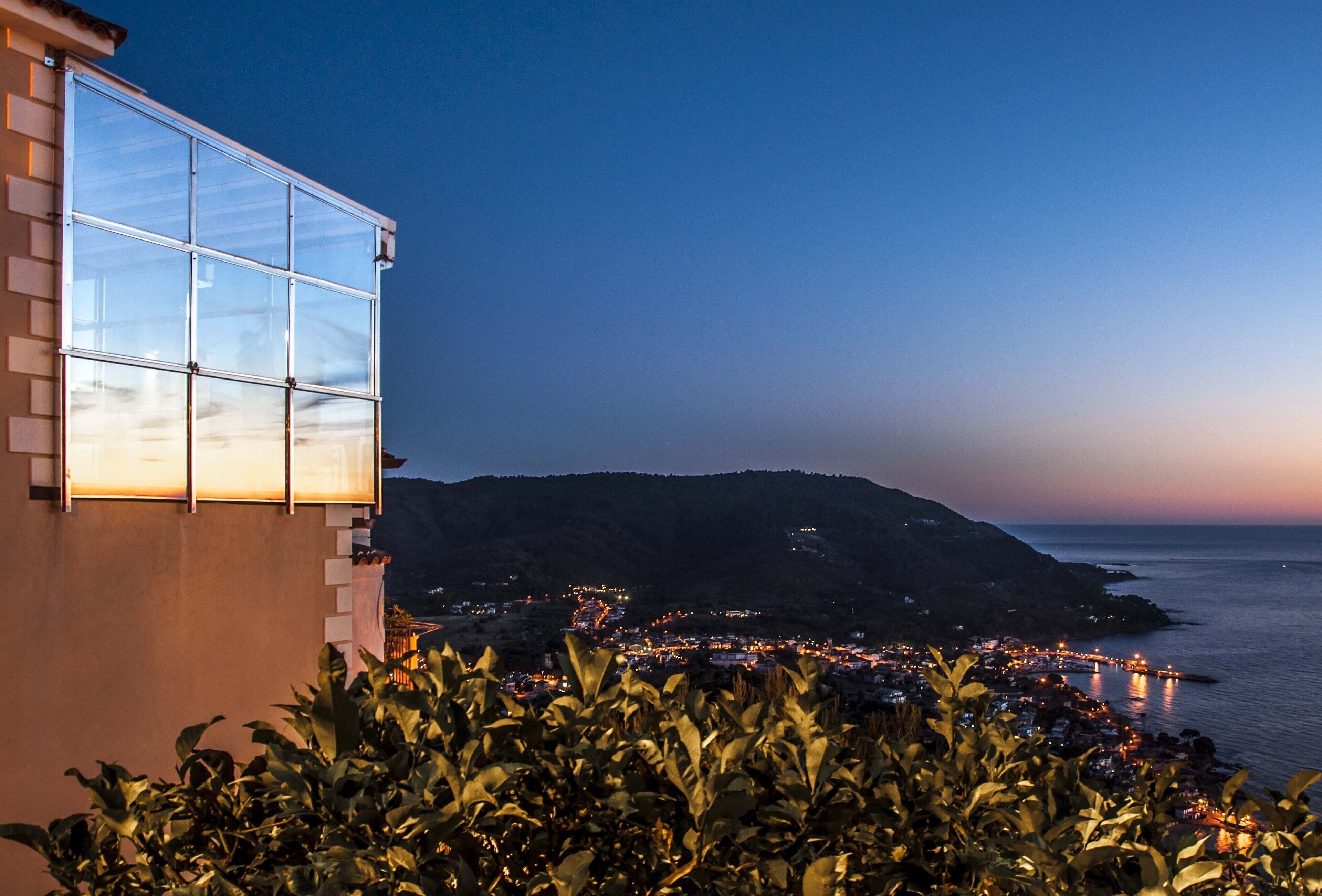Une ville côtière au crépuscule, avec un bâtiment imposant doté de grandes fenêtres.