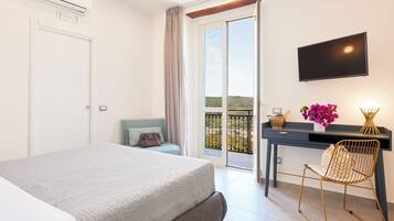 A bedroom with a bed, a desk with a chair, a TV, and a balcony with a view.