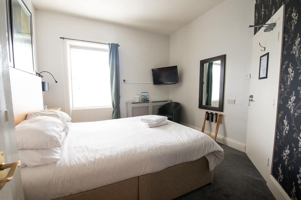 Une chambre d’hôtel dotée d’un grand lit, d’un téléviseur à écran plat fixé au mur, d’un bureau avec une chaise et d’une fenêtre avec des rideaux.