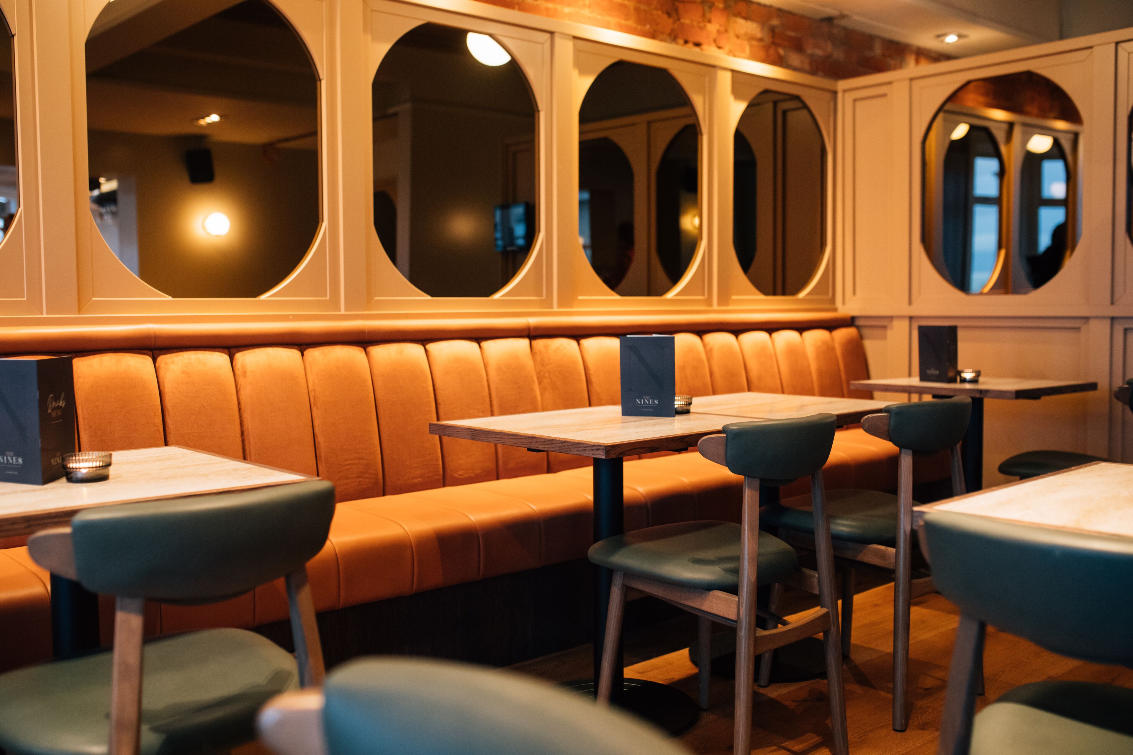 A restaurant with a long, cushioned bench seating area, multiple tables, and chairs.