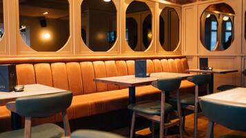 A restaurant with a long, cushioned bench seating area, multiple tables, and chairs.