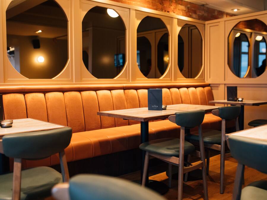 A restaurant with a long, cushioned bench seating area, multiple tables, and chairs.