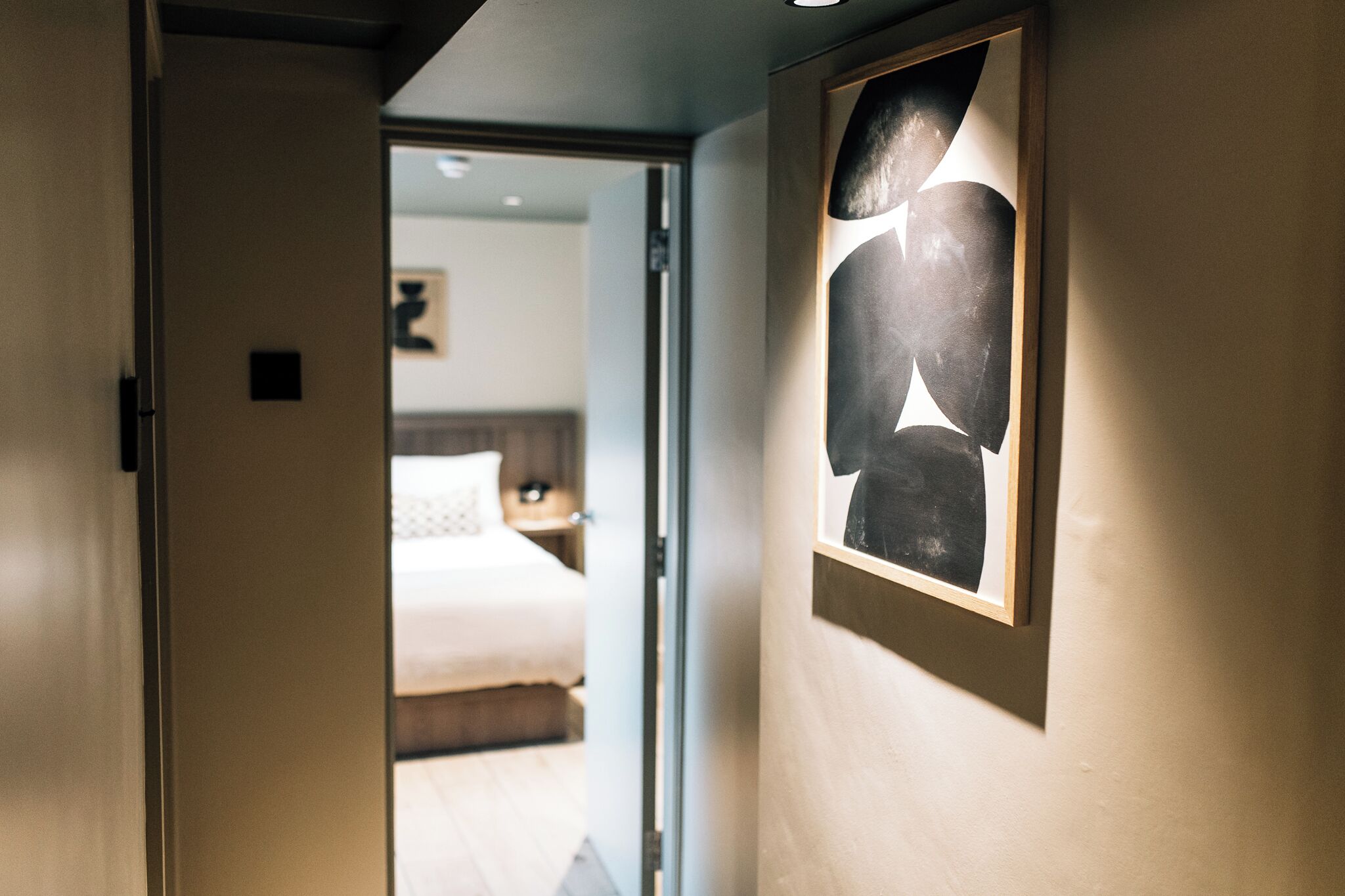 A hallway with a bed, a nightstand, and a framed abstract artwork on the wall.
