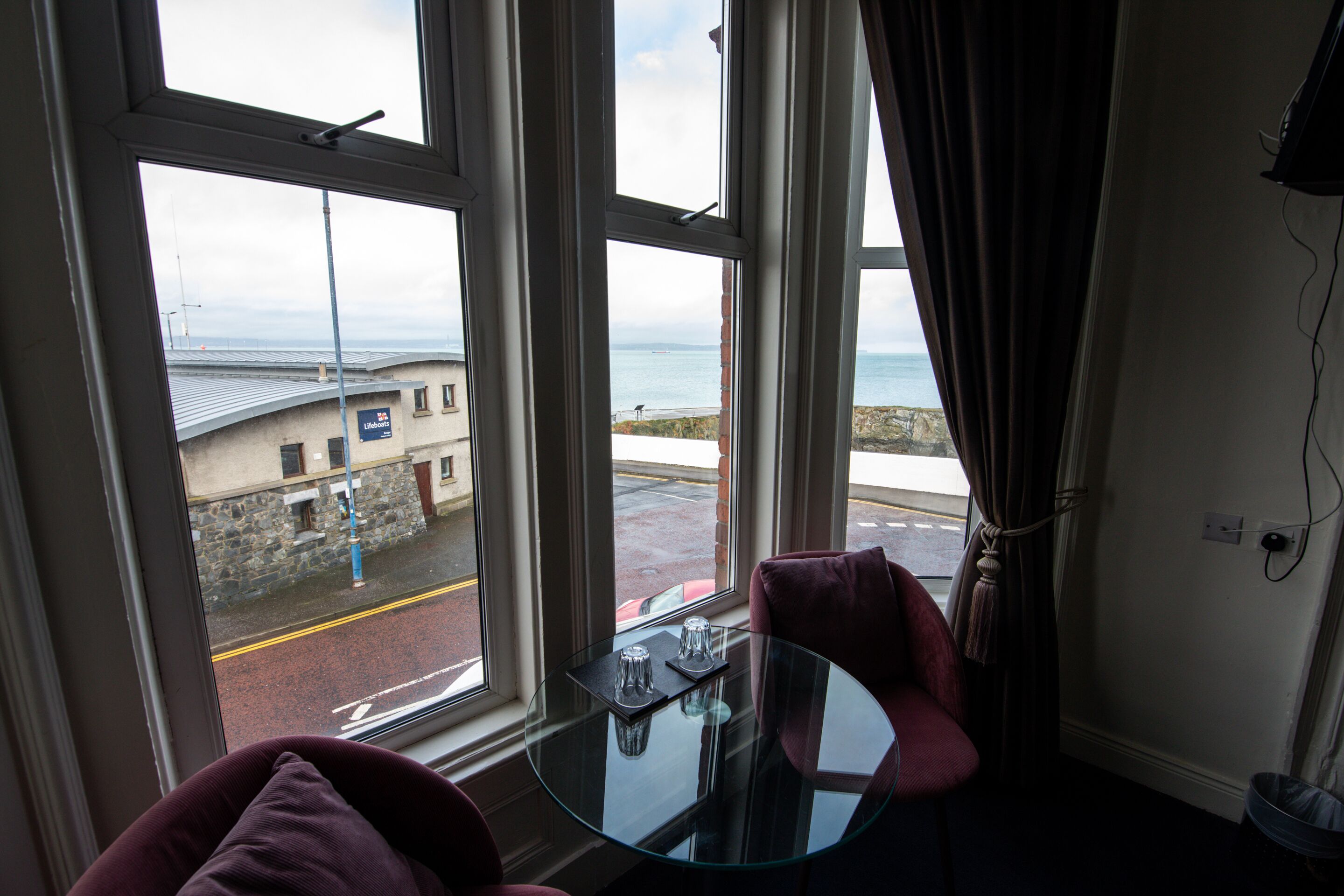 Une pièce avec une table en verre, deux chaises et une vue sur la mer grâce à de grandes fenêtres.