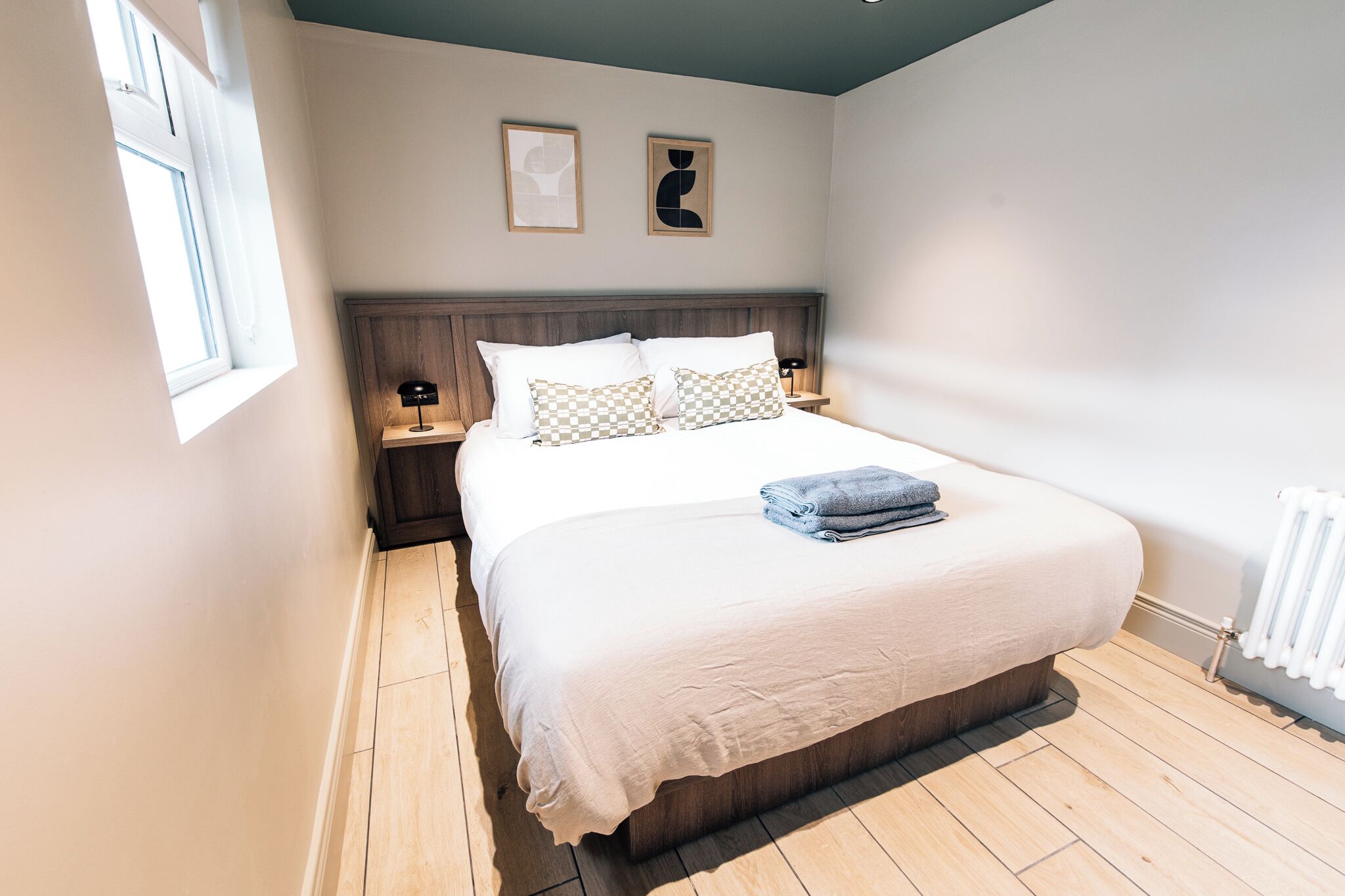 Un dormitorio con una cama grande, dos mesitas de noche, una ventana y un radiador.