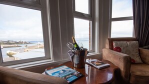 A room with a view of the sea, a cushioned armchair, a wooden table with a bottle of champagne, a glass, and a travel brochure. - The Nines, Bangor Marina (Bangor)