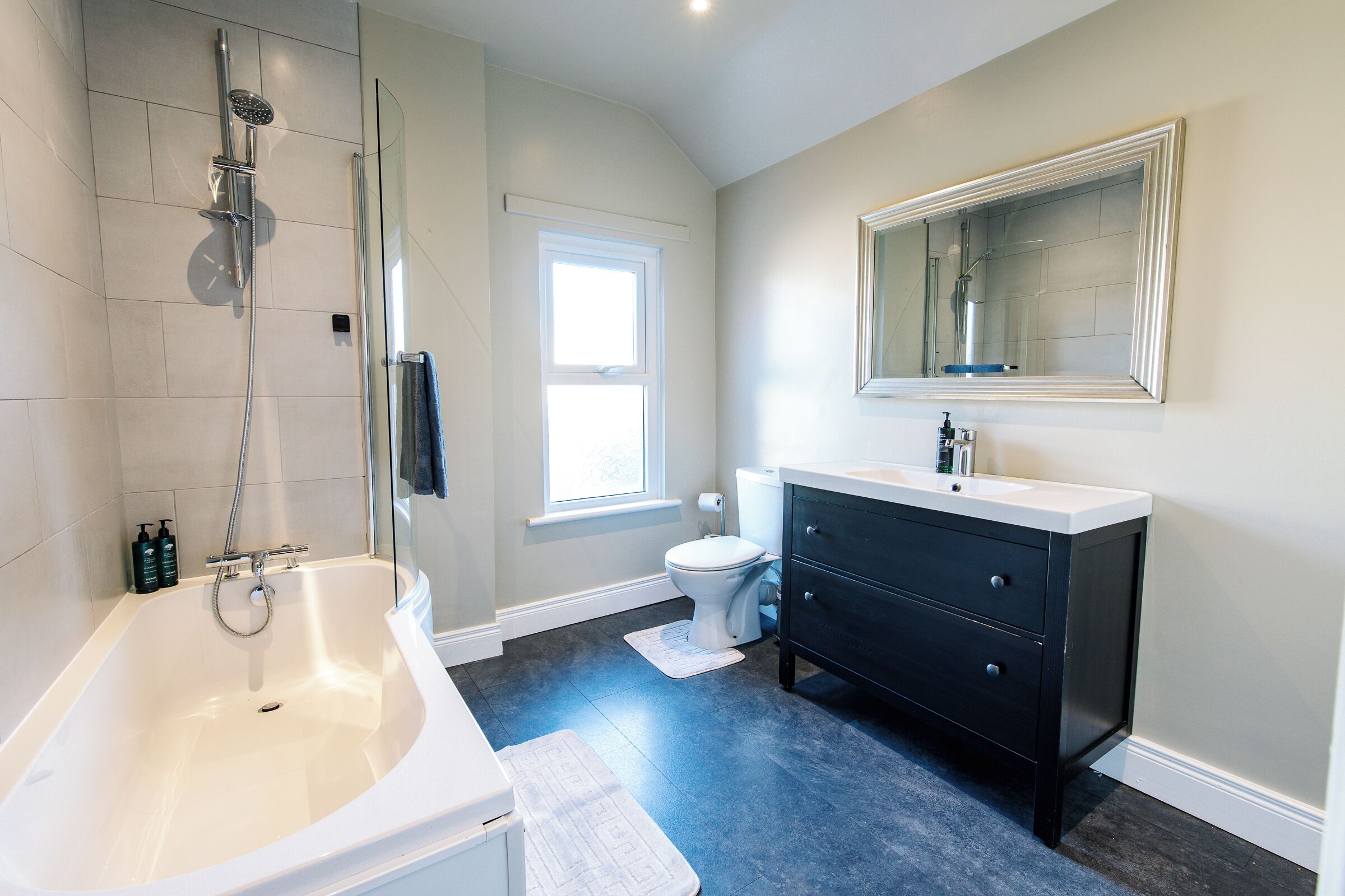 A bathroom with a bathtub, a toilet, a vanity with drawers, a mirror, and a shower with a glass door.