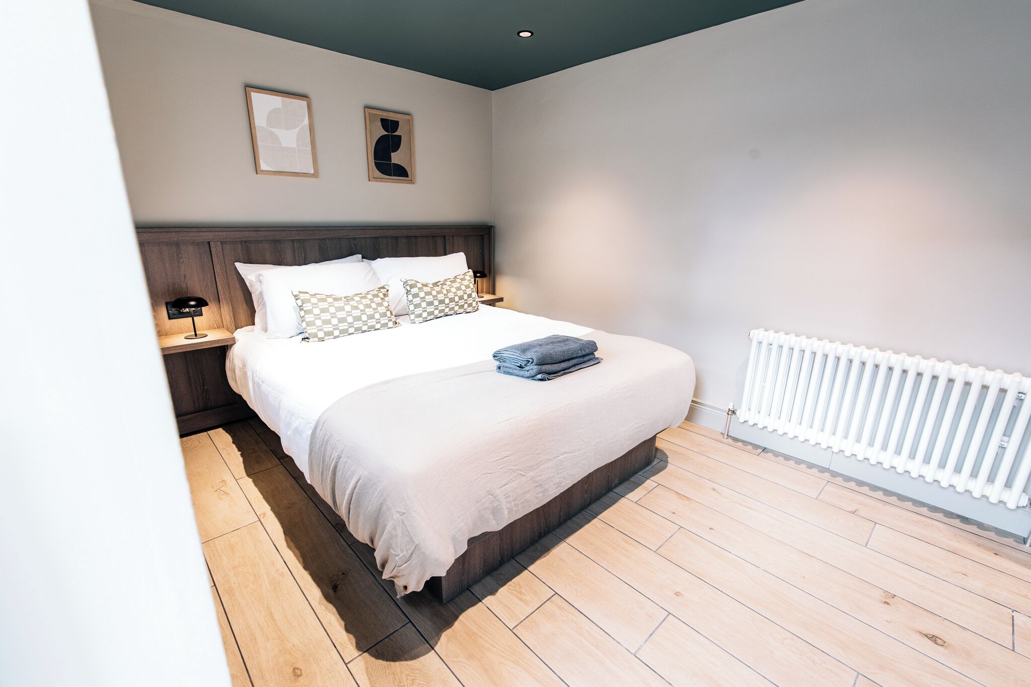 A bedroom with a bed, nightstands, a wall-mounted radiator, and two framed pictures.