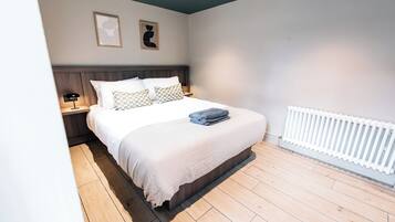 A bedroom with a bed, nightstands, a wall-mounted radiator, and two framed pictures.