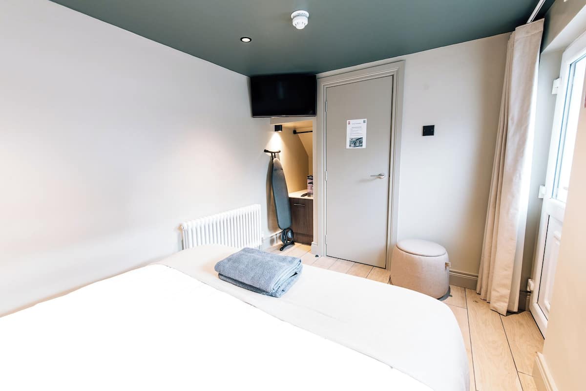 Une chambre d’hôtel avec un lit, un téléviseur fixé au mur, une porte et une fenêtre avec des rideaux.