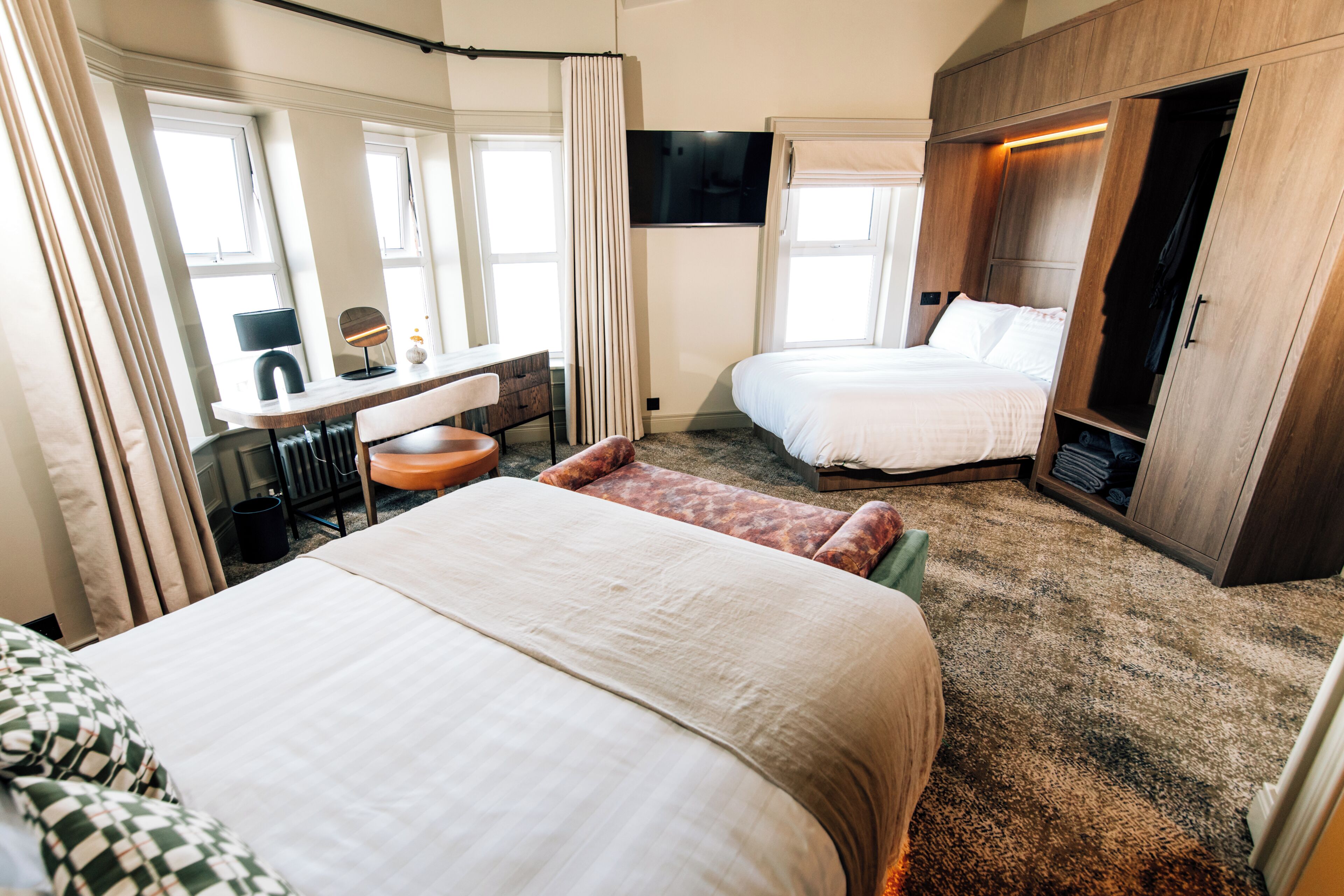 Ein Hotelzimmer mit zwei Betten, einem Schreibtisch mit Stuhl, einem Fernseher und einem Kleiderschrank.