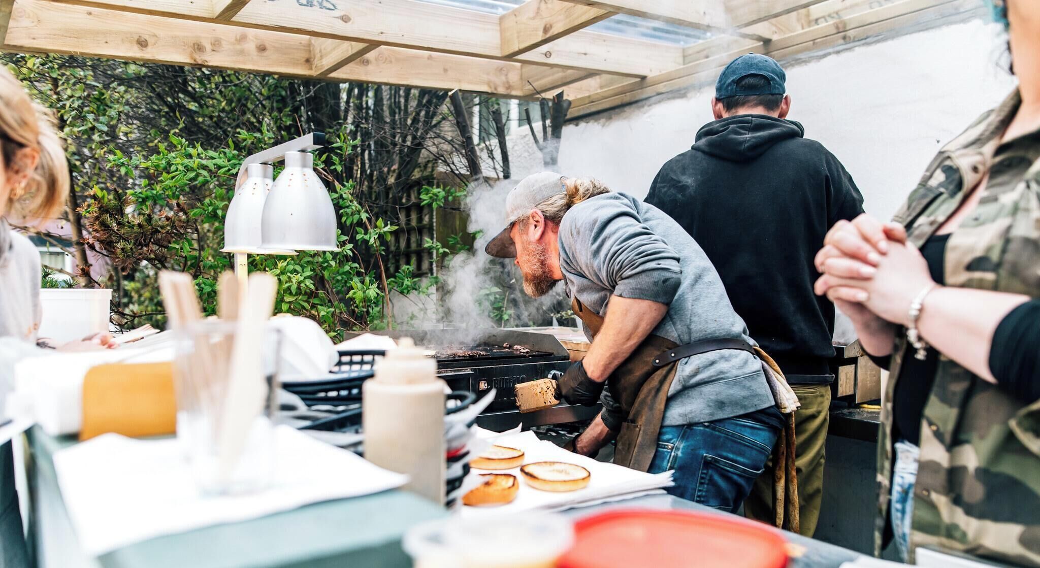 An outdoor cooking area with a grill, a table with food items, and a person cooking.