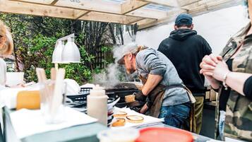 An outdoor cooking area with a grill, a table with food items, and a person cooking.