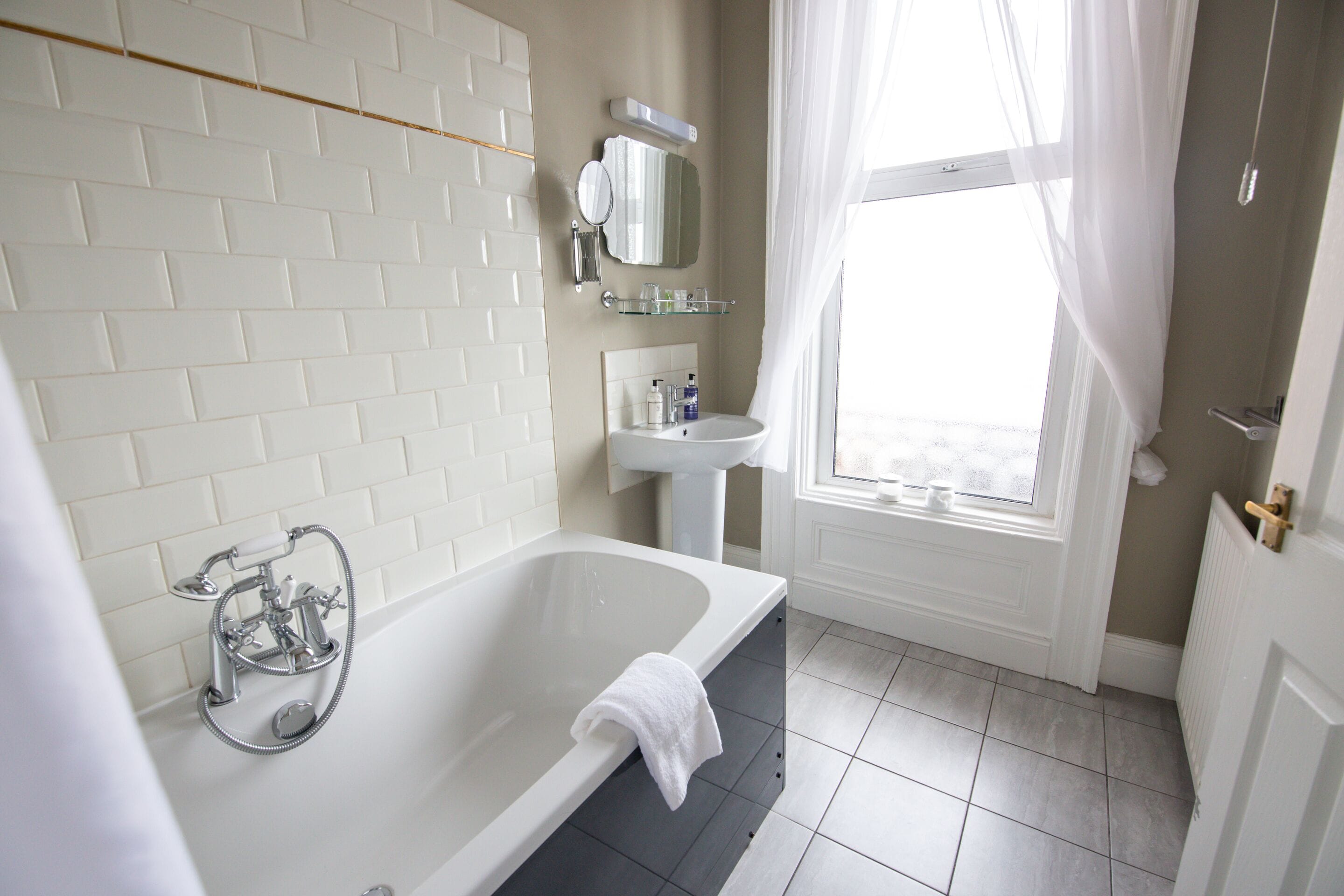 Un bany modern amb una banyera autònoma, un lavabo i una finestra amb cortines.