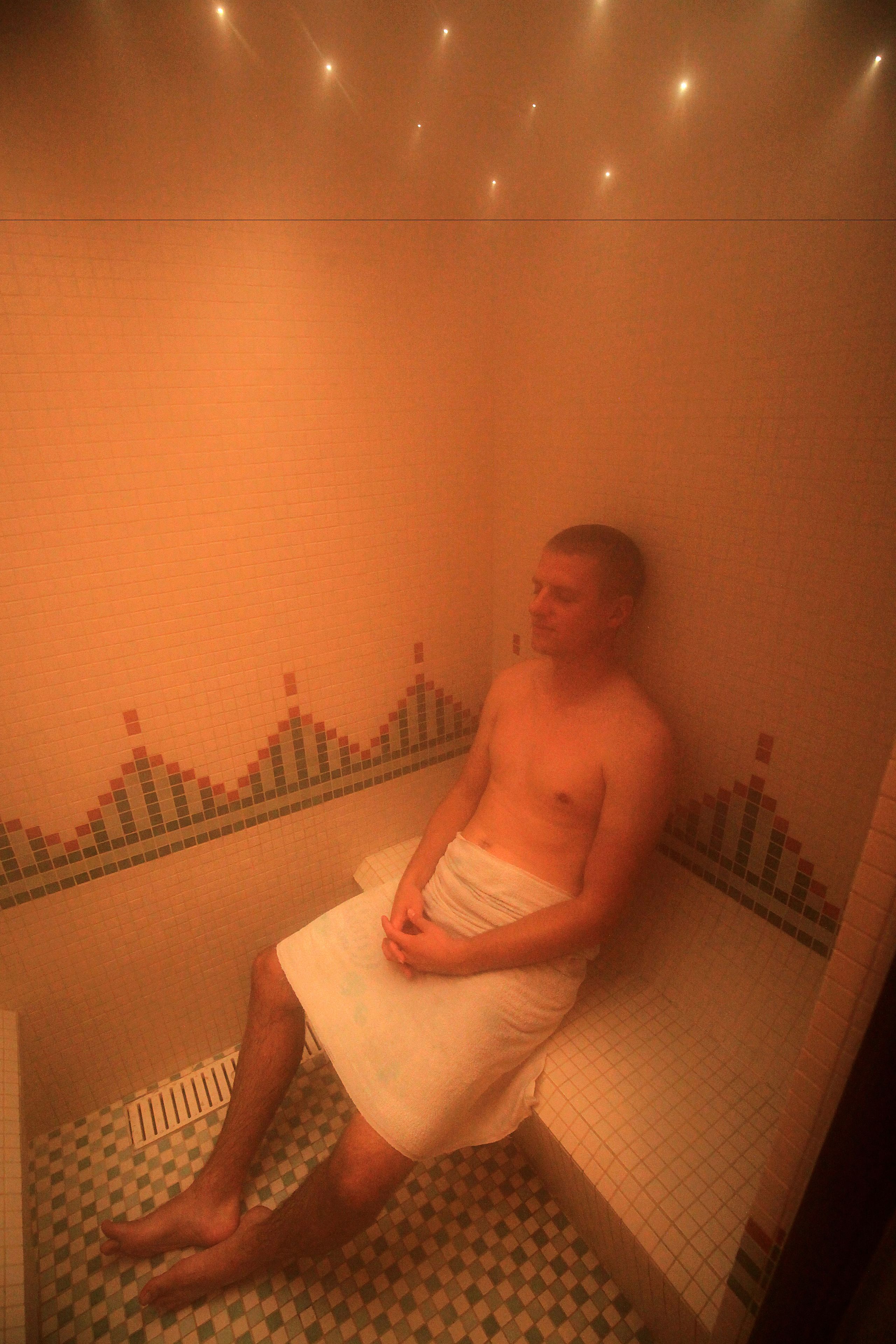 A person sitting on a bench in a room with patterned tile flooring and walls.