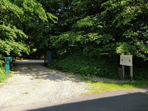 Un chemin de gravier mène à un portail entouré d’un feuillage verdoyant et dense. Une pancarte indique : « LA PETITE BRUYÈRE DE RENAIS ».