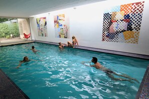 Une piscine intérieure à l’eau d’un bleu cristallin, entourée de murs ornés d’œuvres d’art abstrait aux couleurs vives.