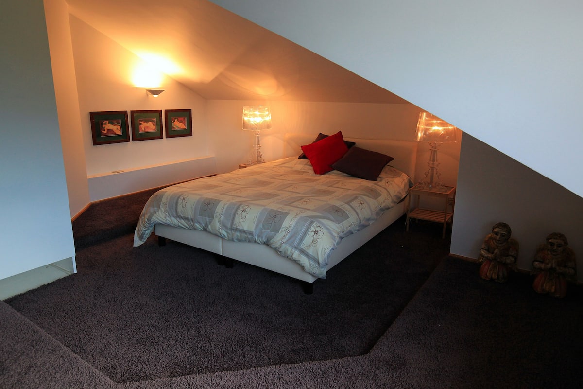 A bedroom with a bed, two wall-mounted lamps, and three framed pictures on the wall.