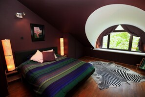 Une chambre avec un grand lit, une fenêtre avec des rideaux, un tapis à motifs zébrés et un luminaire fixé au mur.